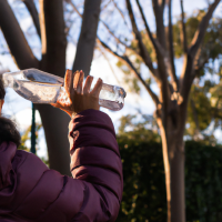 someone drinking water at the park, wearing clothes like they had been exercising with a light spring season feeling and lots of activity at the park around